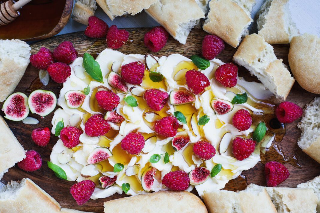 Flatlay of Butter board topped with fresh raspberries, figs, sliced almonds, basil leaves