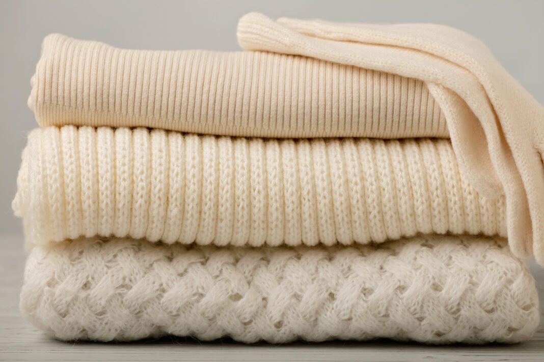 Pile of knitted clothes (sweaters, scarves, pullovers) white and beige colors.