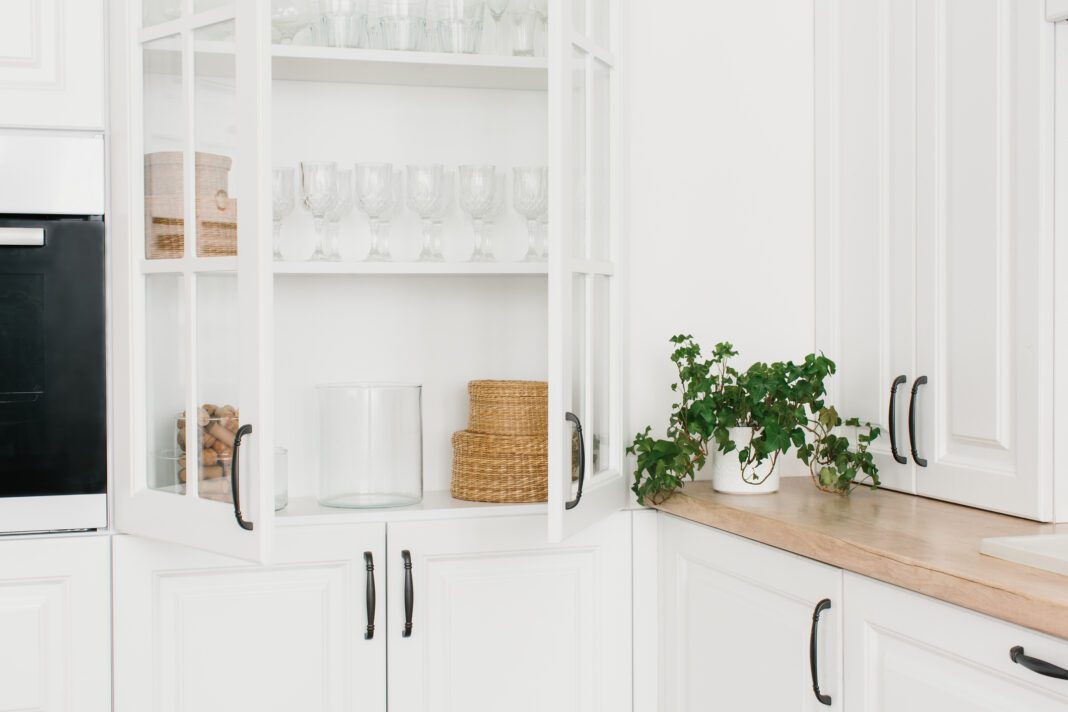 Opened white glass cabinet with clean dishes and decor. Scandinavian style kitchen interior. Organization of storage in kitchen.