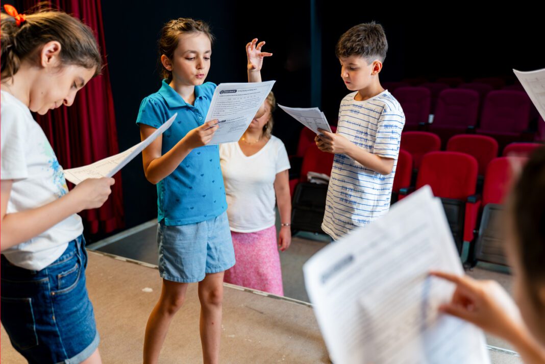 Group of children enjoying drama club rehearsal. They are reading script with their drama teacher.