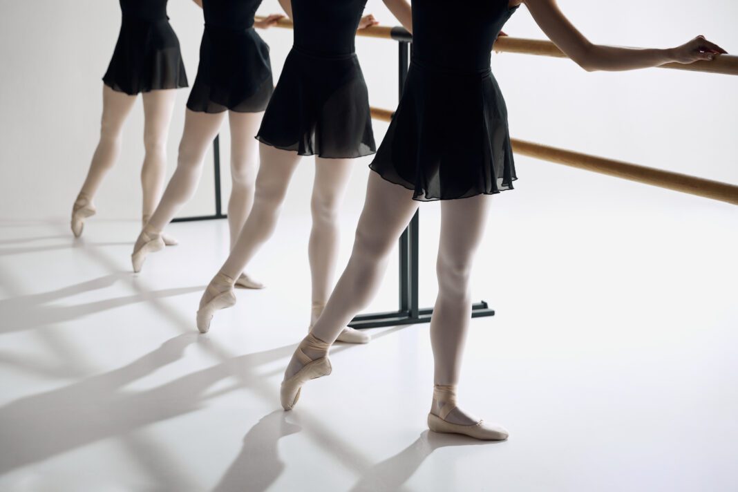 Elegance on pointe. Cropped image of female ballet dancer standing in a row at barre, practicing against grey studio background