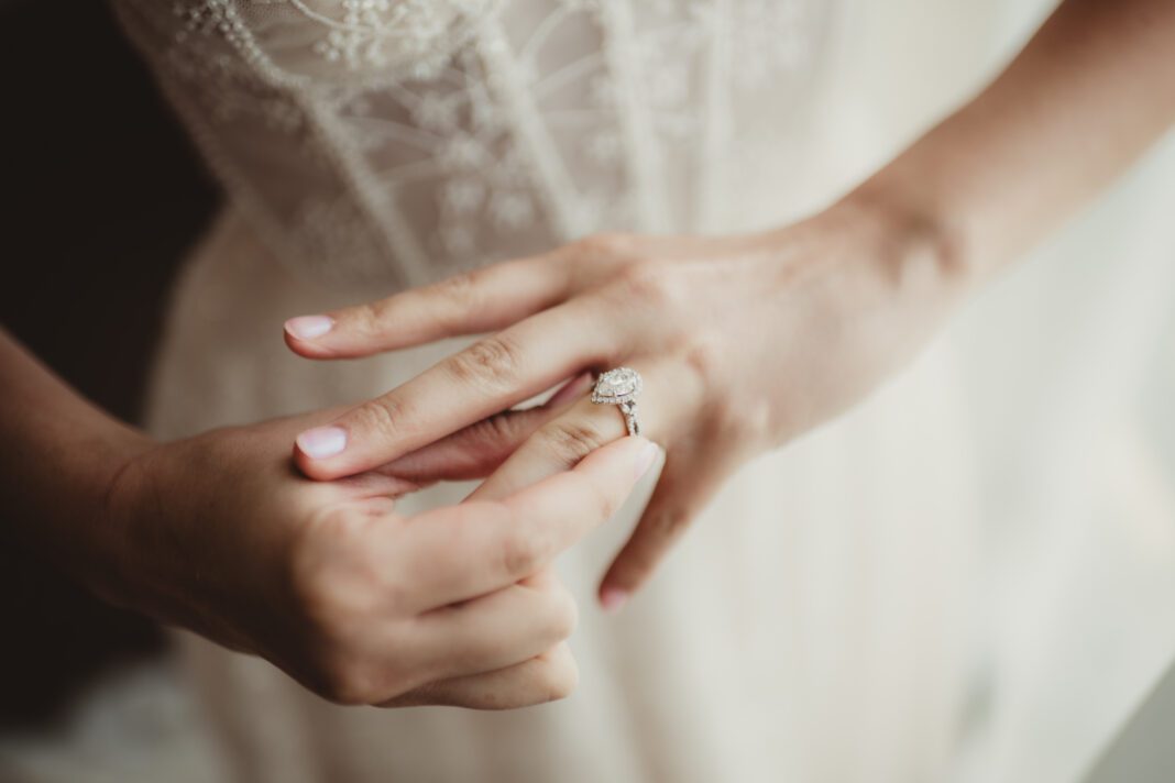 Bride in wedding dress putting on teardrop shaped diamond engagement ring